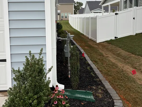 A mulch bed with a stone border wrapping a corner between house and fence.