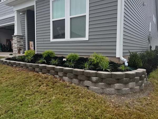 A raised stone retaining wall holding a planted bed against the house.
