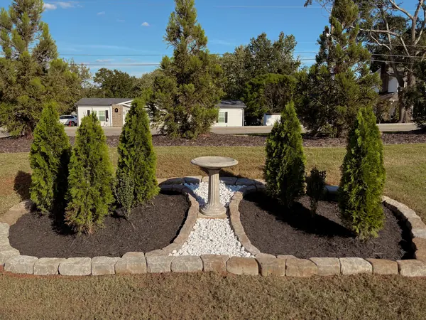 Twin stone-edged mulch beds flanking a birdbath on a gravel bed.